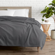 A polar fleece blanket on a bed next to a table and a large plant