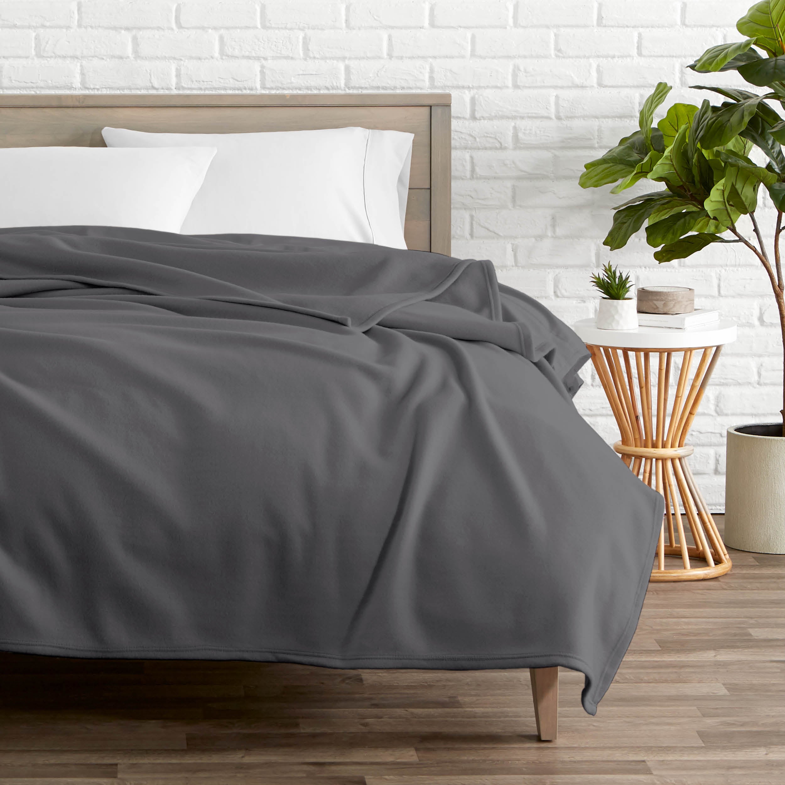 A polar fleece blanket on a bed next to a table and a large plant