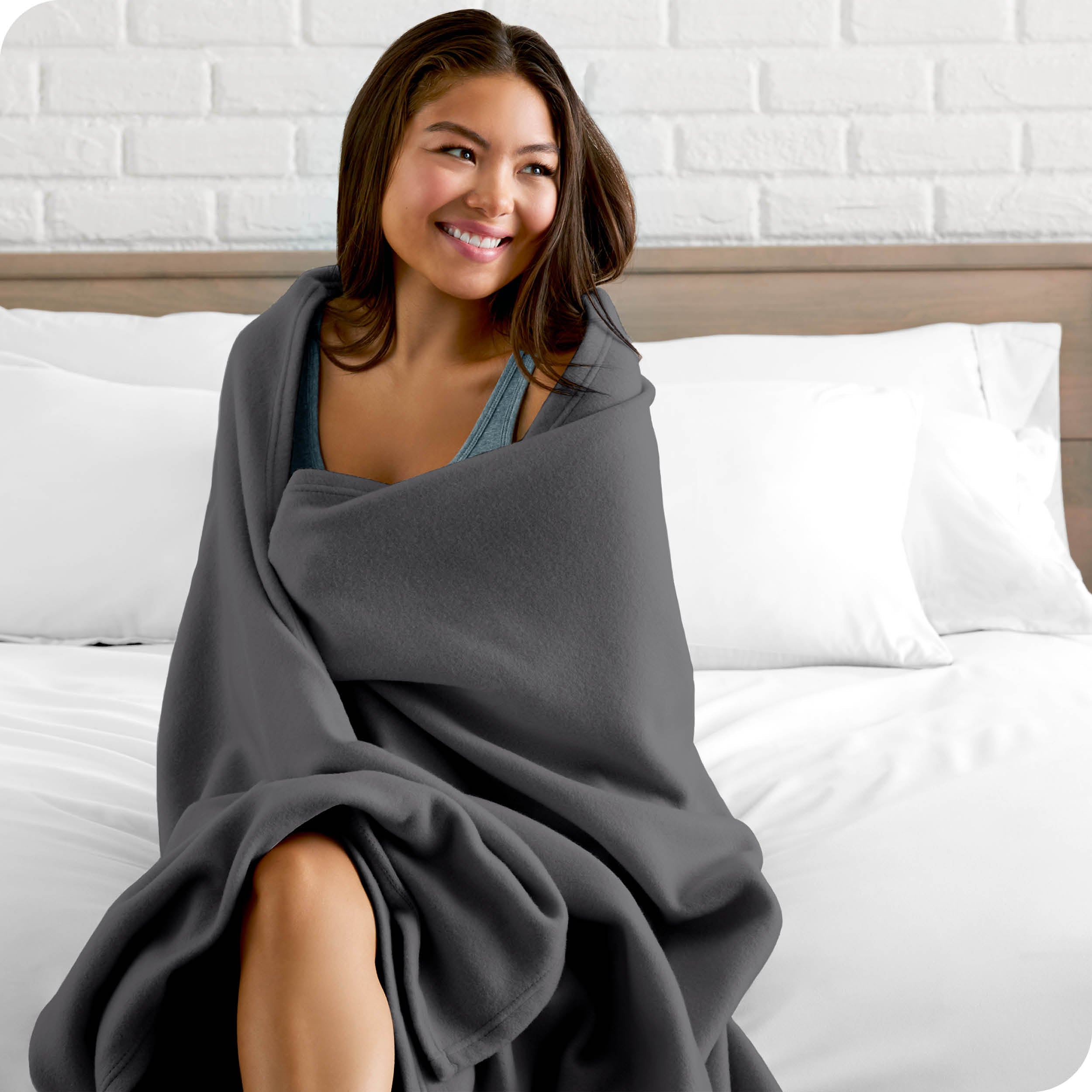 A woman sitting at the end of a bed with a fleece blanket wrapped around her shoulders
