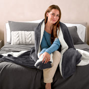 Woman cuddling with a sherpa blanket while sitting on the end of a bed