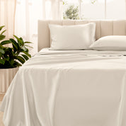 Organic sateen bedding on a bed with a beige headboard and plant in the corner.