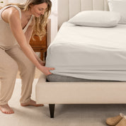 A women is putting on the percale fitted sheet on the bed