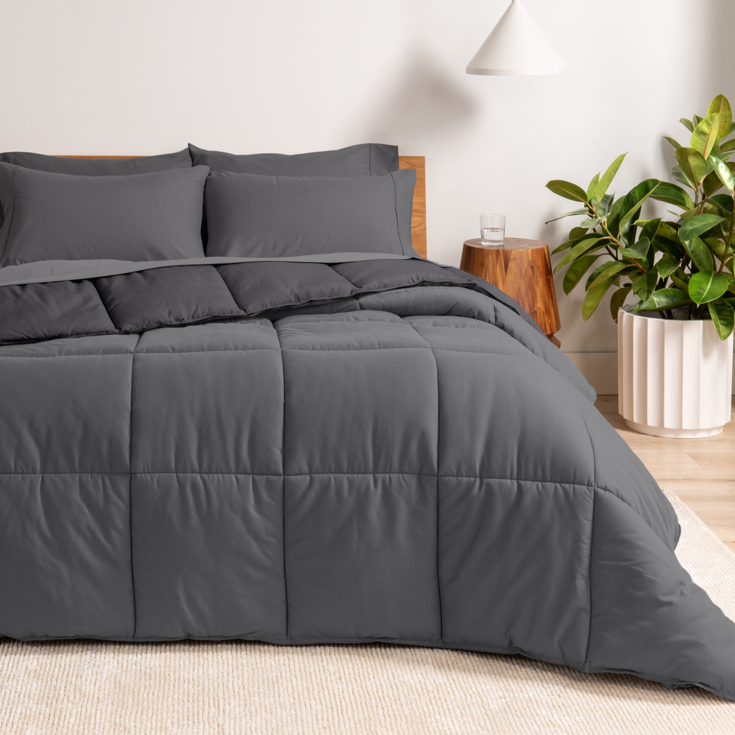 A wooden bed frame with a reversible comforter and sheet set on the mattress in a bright warm room.