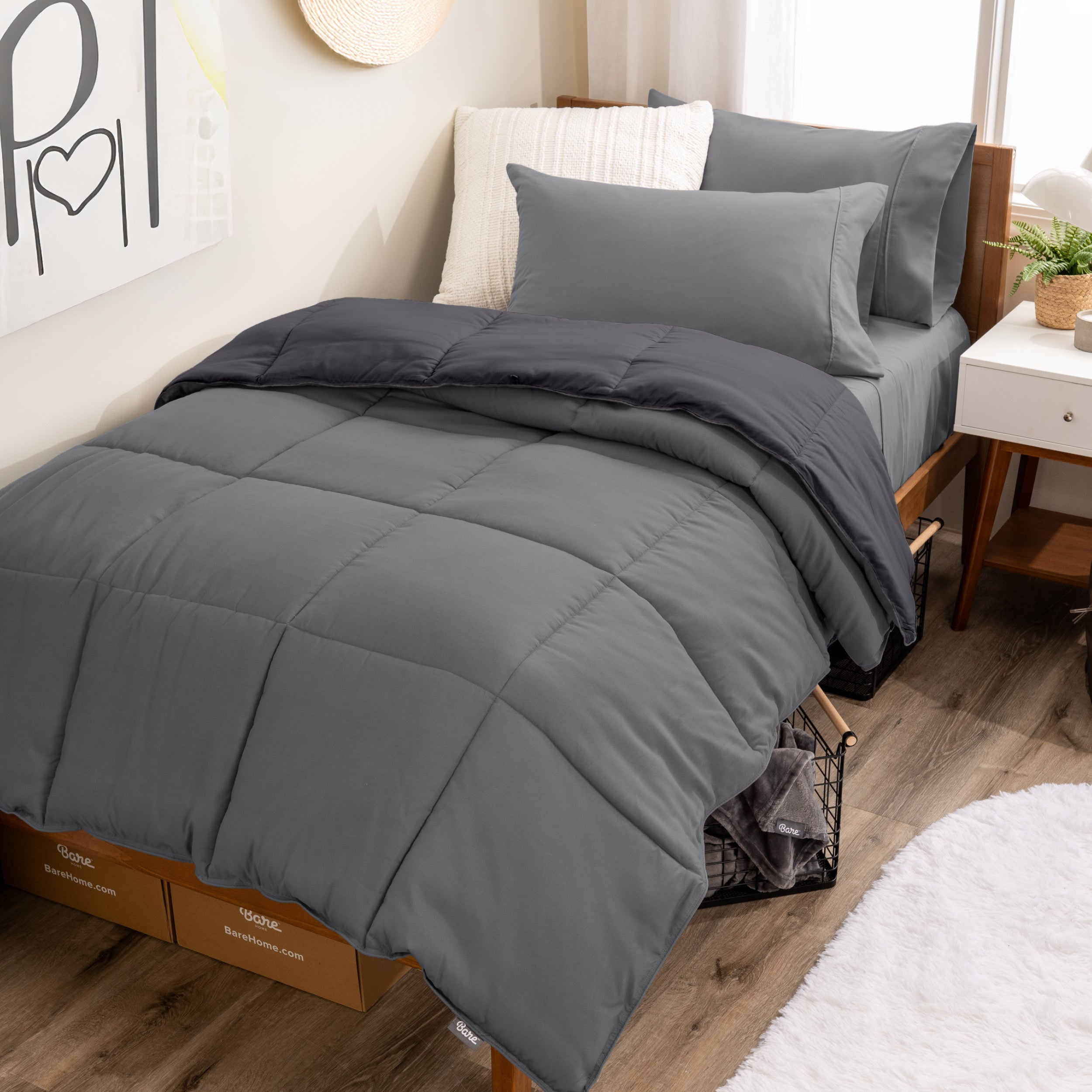 A wooden bed frame with a reversible comforter and sheet set on the mattress in a dorm style room.