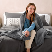Woman cuddling with a sherpa blanket while sitting on the end of a bed