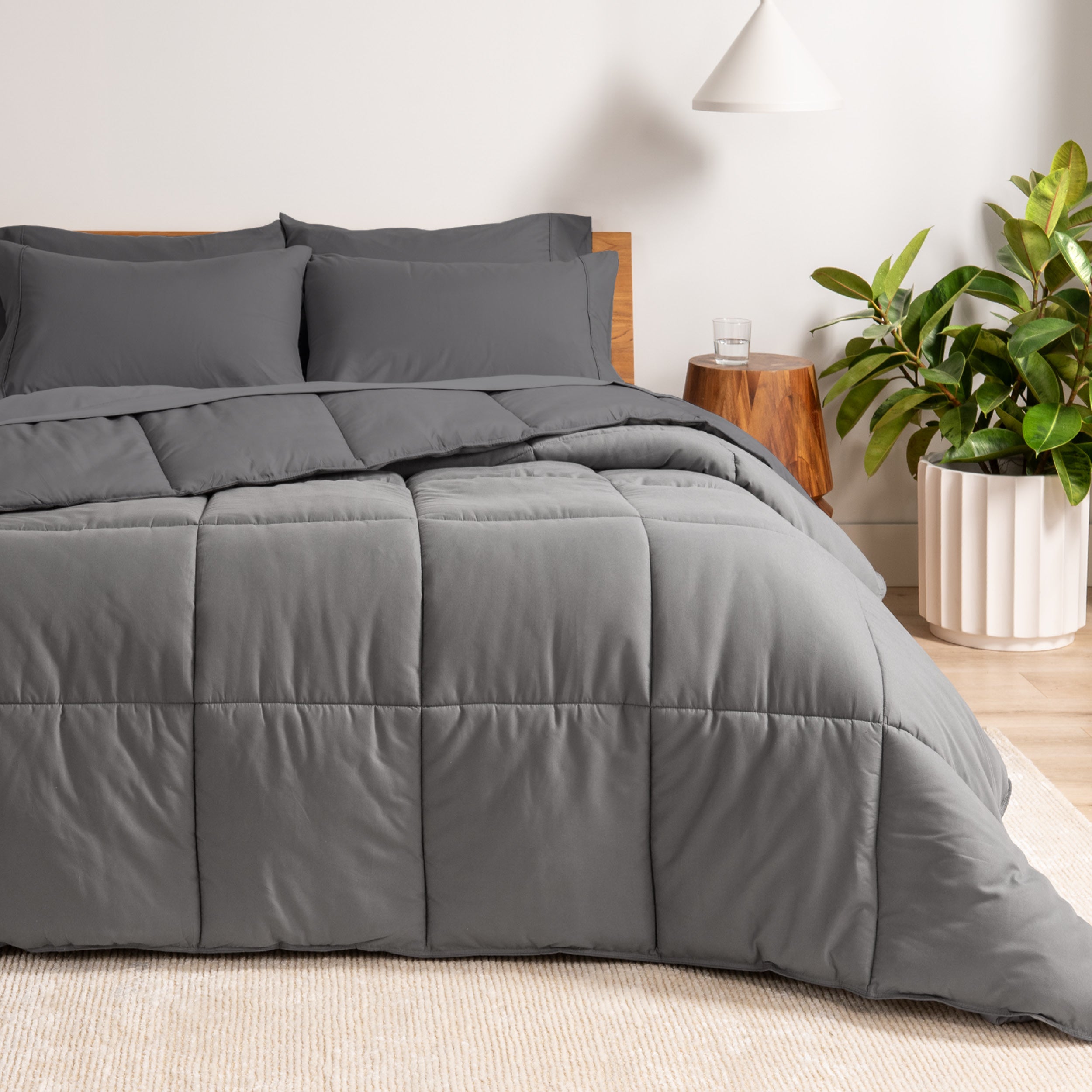 A wooden bed frame with a reversible comforter and sheet set on the mattress in a bright warm room.