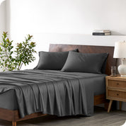 Modern bedroom with a bed against a white wall with a nightstand next to the bed. The bed has bamboo sheets draped over it.