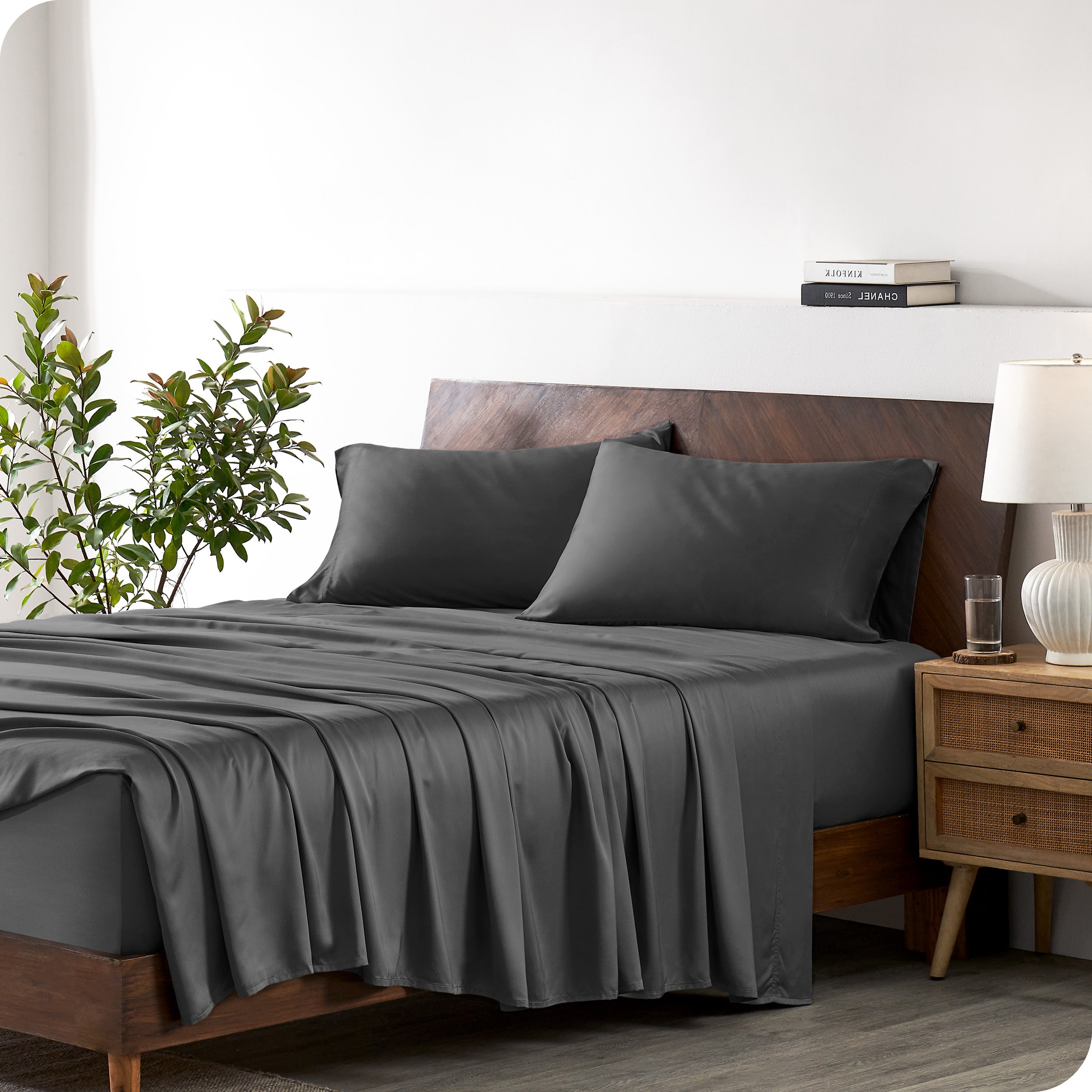 Modern bedroom with a bed against a white wall with a nightstand next to the bed. The bed has bamboo sheets draped over it.
