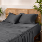 Bamboo bed sheets and pillowcases on a bed with a wicker headboard and plants in the background.