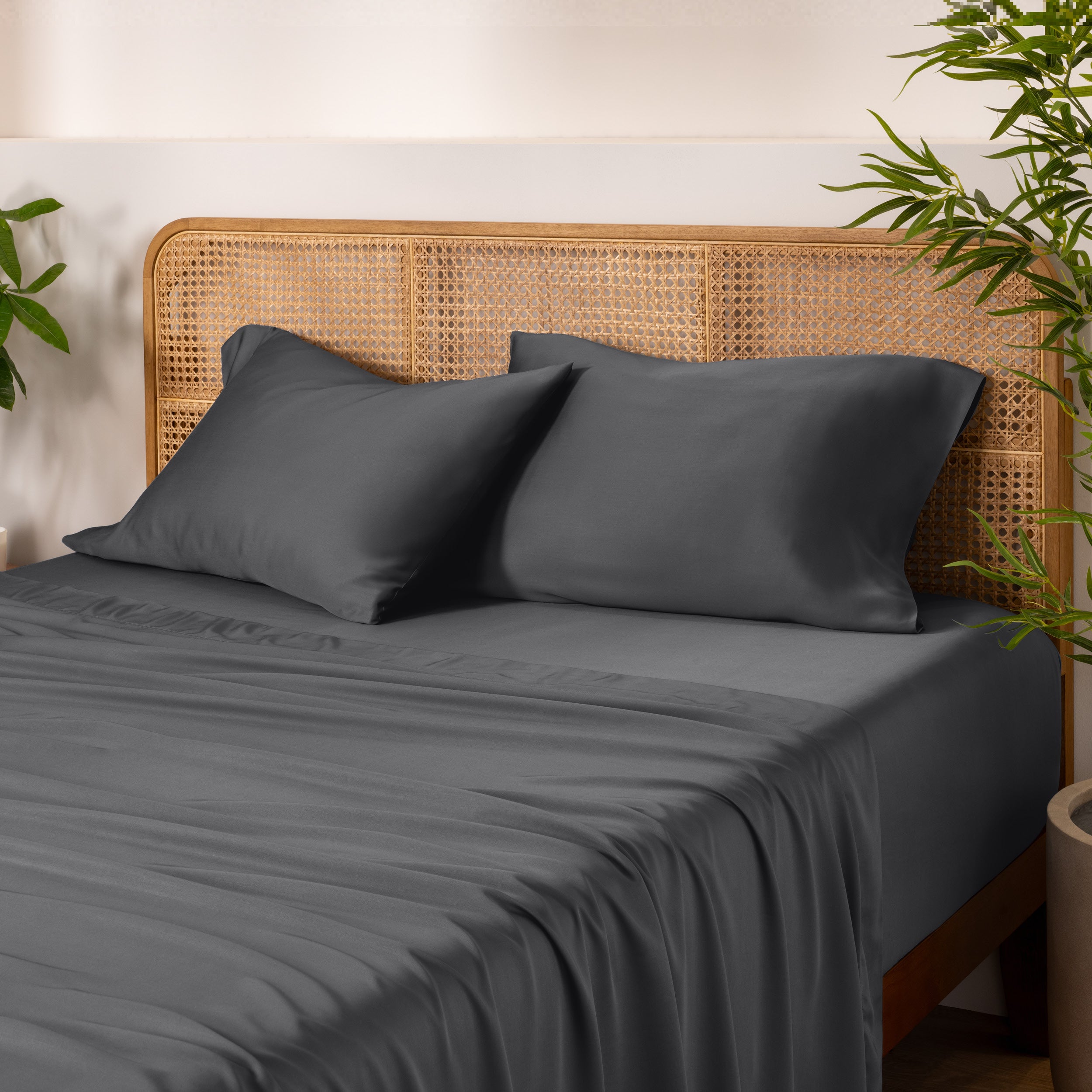 Bamboo bed sheets and pillowcases on a bed with a wicker headboard and plants in the background.