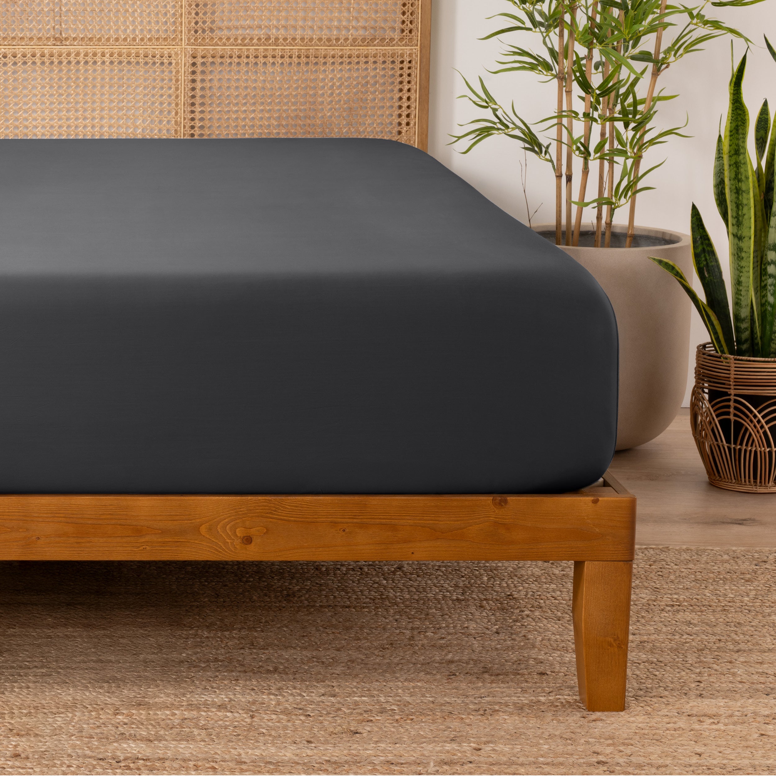 Bamboo fitted sheet on a wooden bed with plants in the background