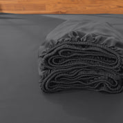 Folded fitted sheet on a bed with a wooden headboard.