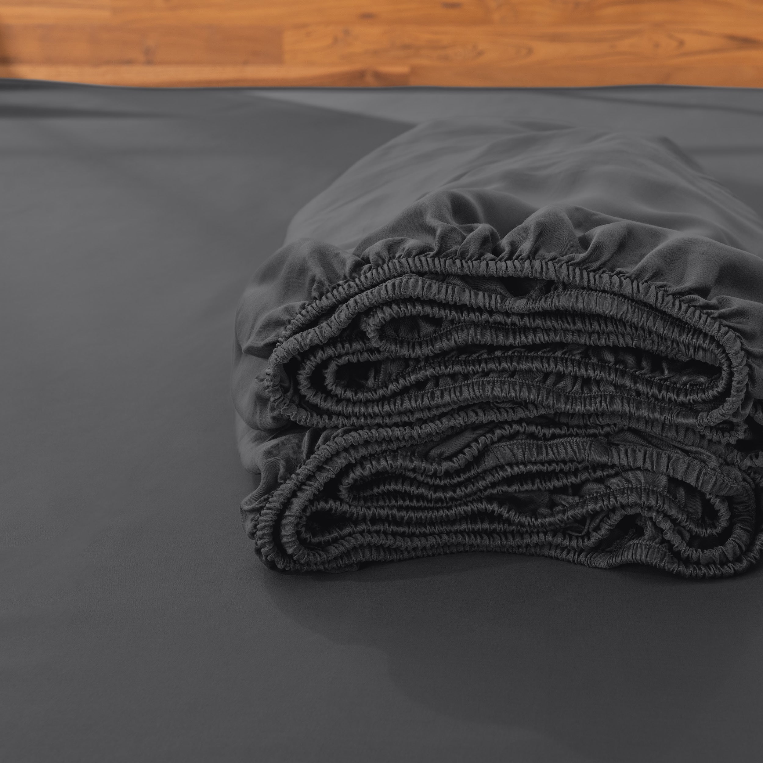 Folded fitted sheet on a bed with a wooden headboard.