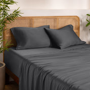 Bamboo bed sheets and pillowcases on a bed with a wicker headboard in a room with plants.