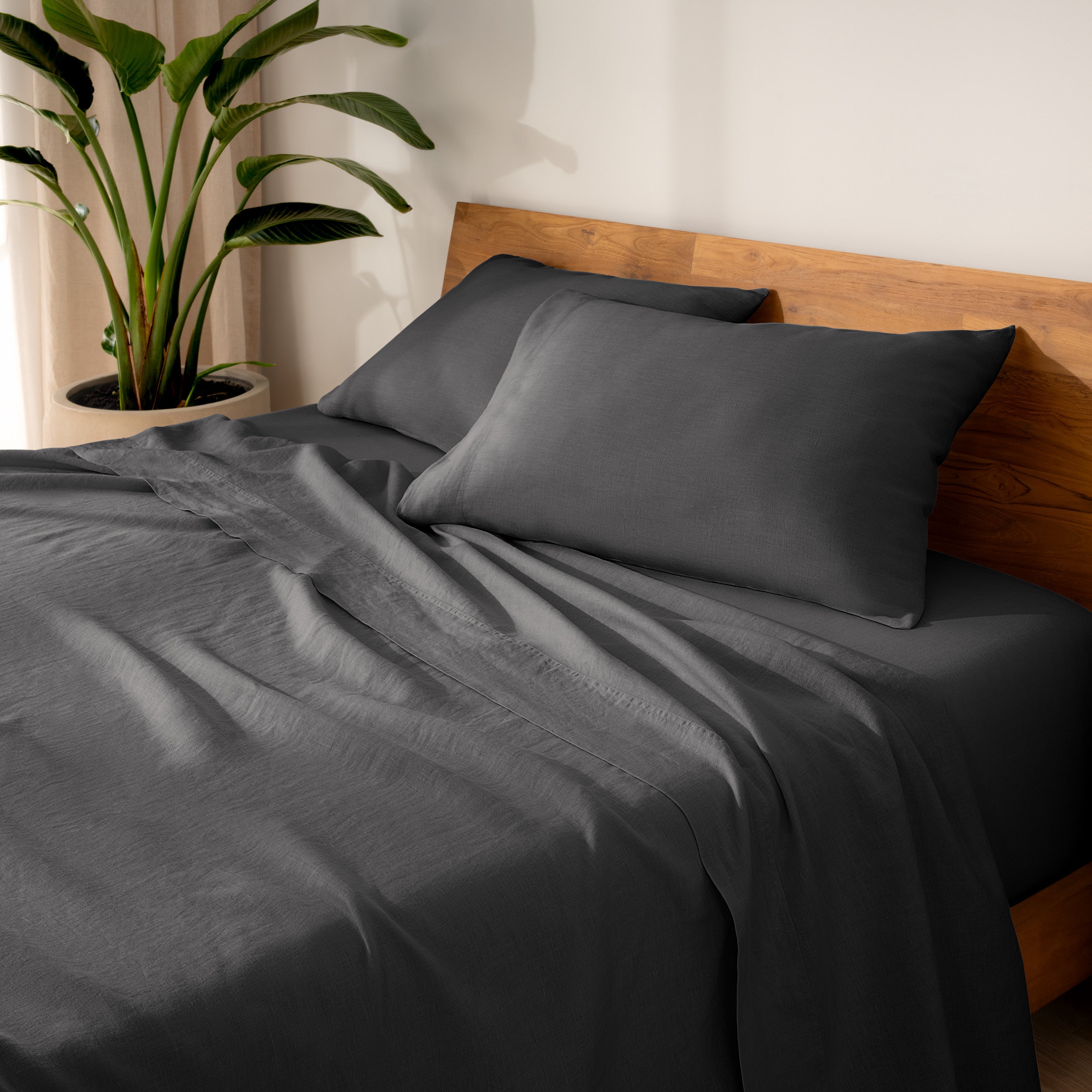 Linen bed sheets and pillows on a wooden bed with a plant in the background