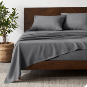 Dark wooden bed frame with grey linen sheets on the mattress