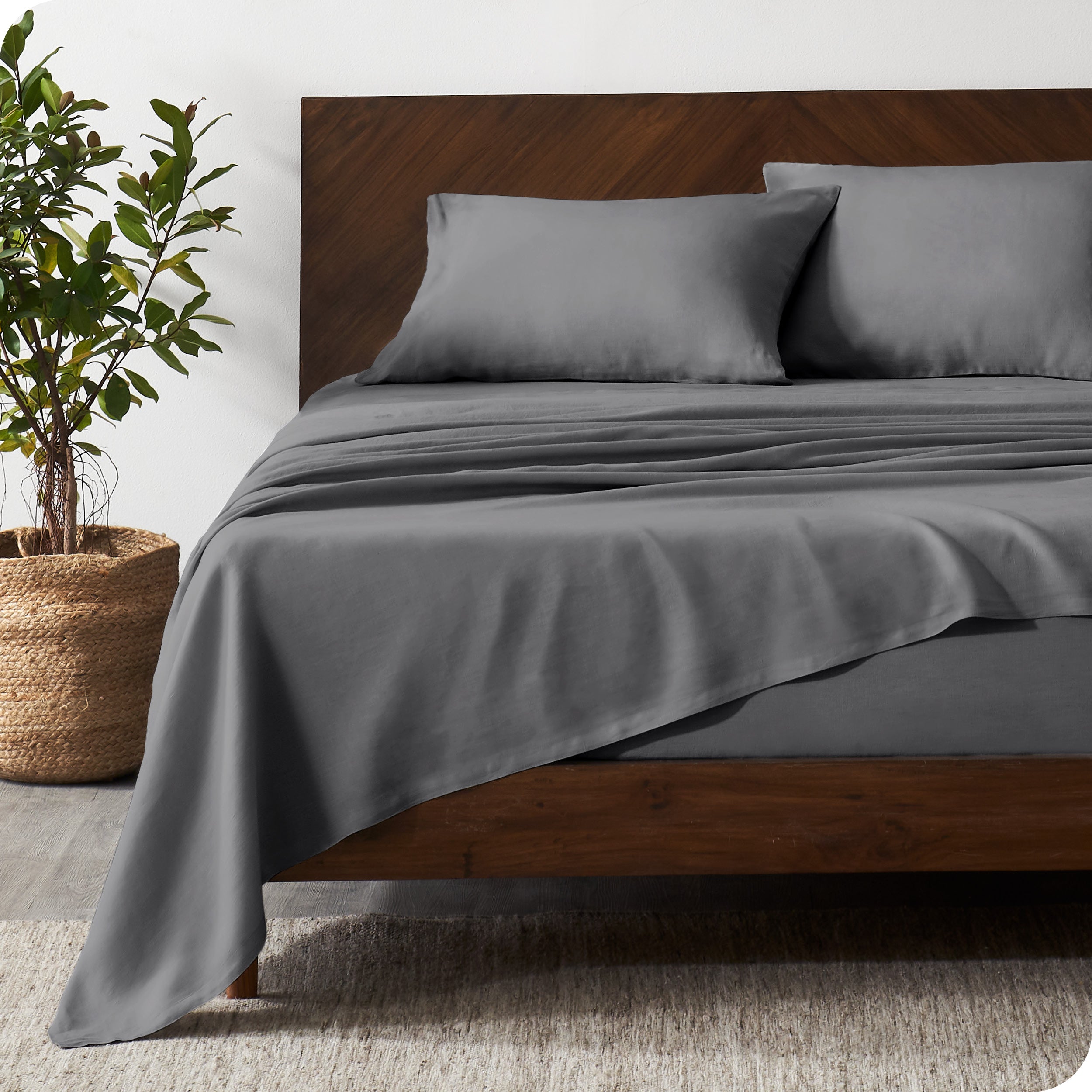 Dark wooden bed frame with grey linen sheets on the mattress