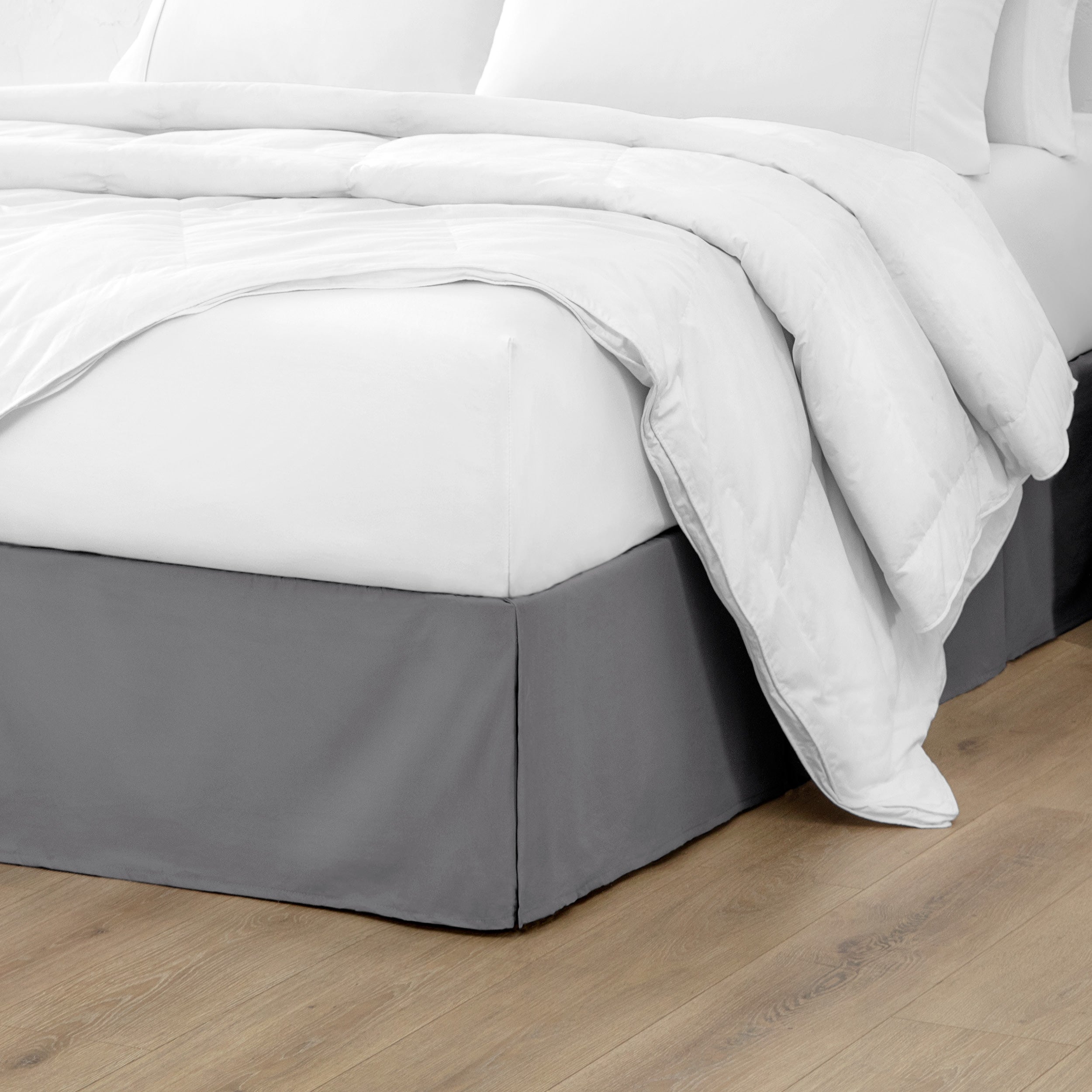 The corner of a bed with a bed skirt and comforter on it