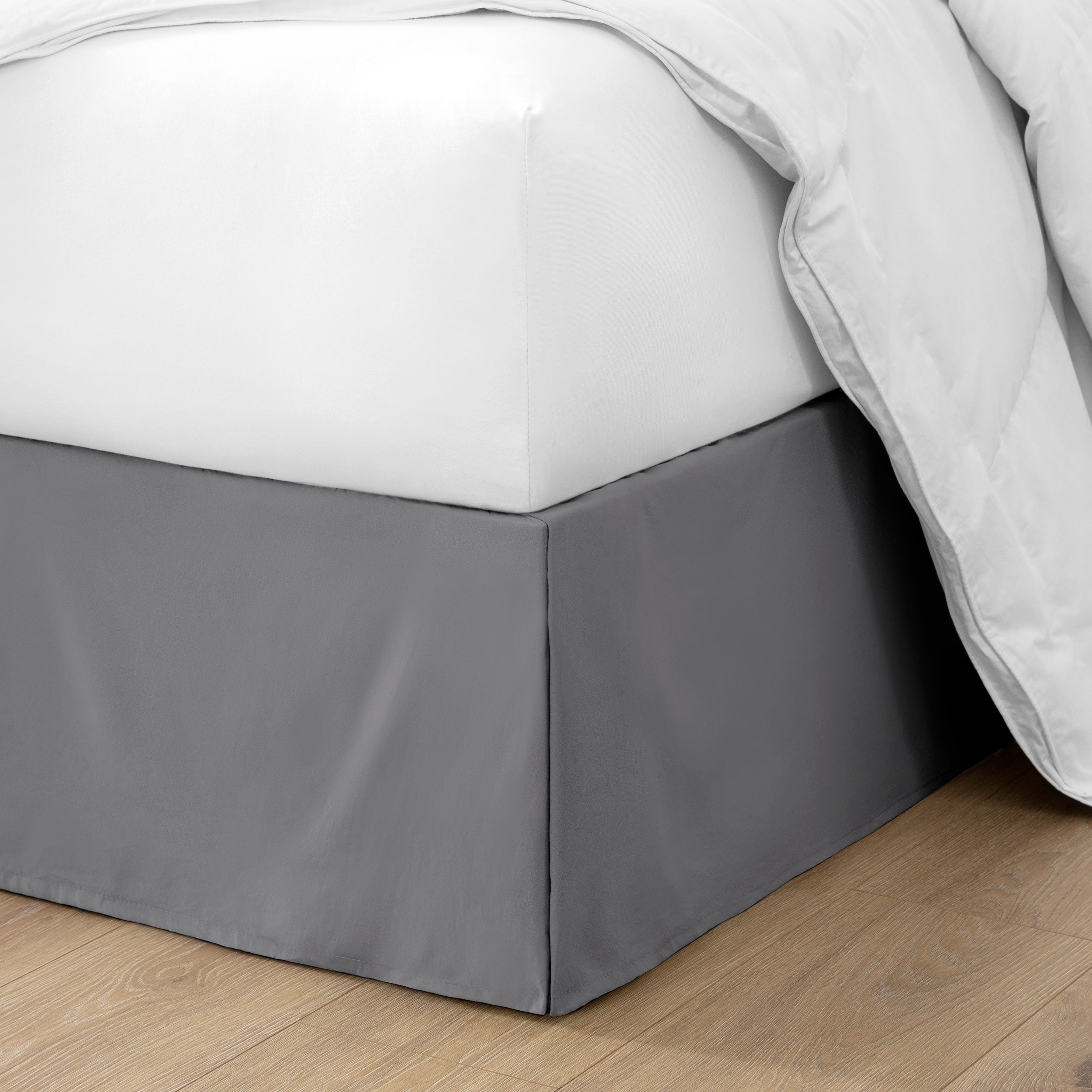 The corner of a bed with a bed skirt and comforter on it