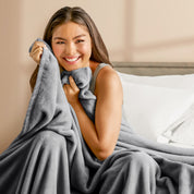 A woman sitting on a bed wrapped in a microplush blanket