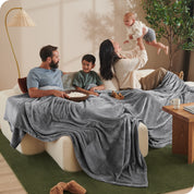 A family sitting on a couch with a giant microplush blanket covering them