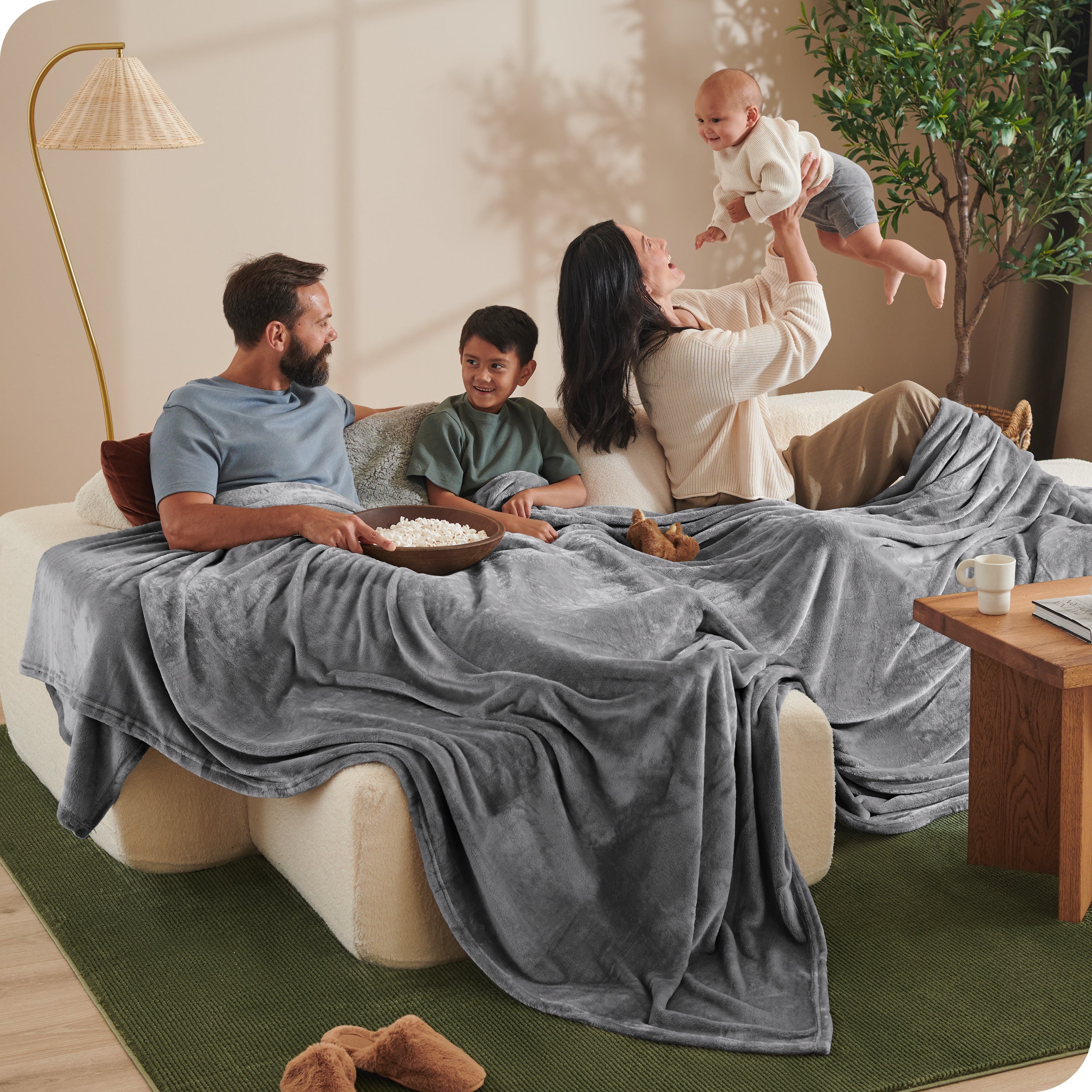 A family sitting on a couch with a giant microplush blanket covering them