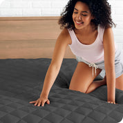 A woman is pushed her hand down on a quilted mattress pad on the bed