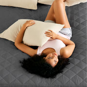 A women is laying on the bed with quilted mattress pad from above.