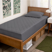 A bed with a wooden bed frame with a quilted mattress pad on.