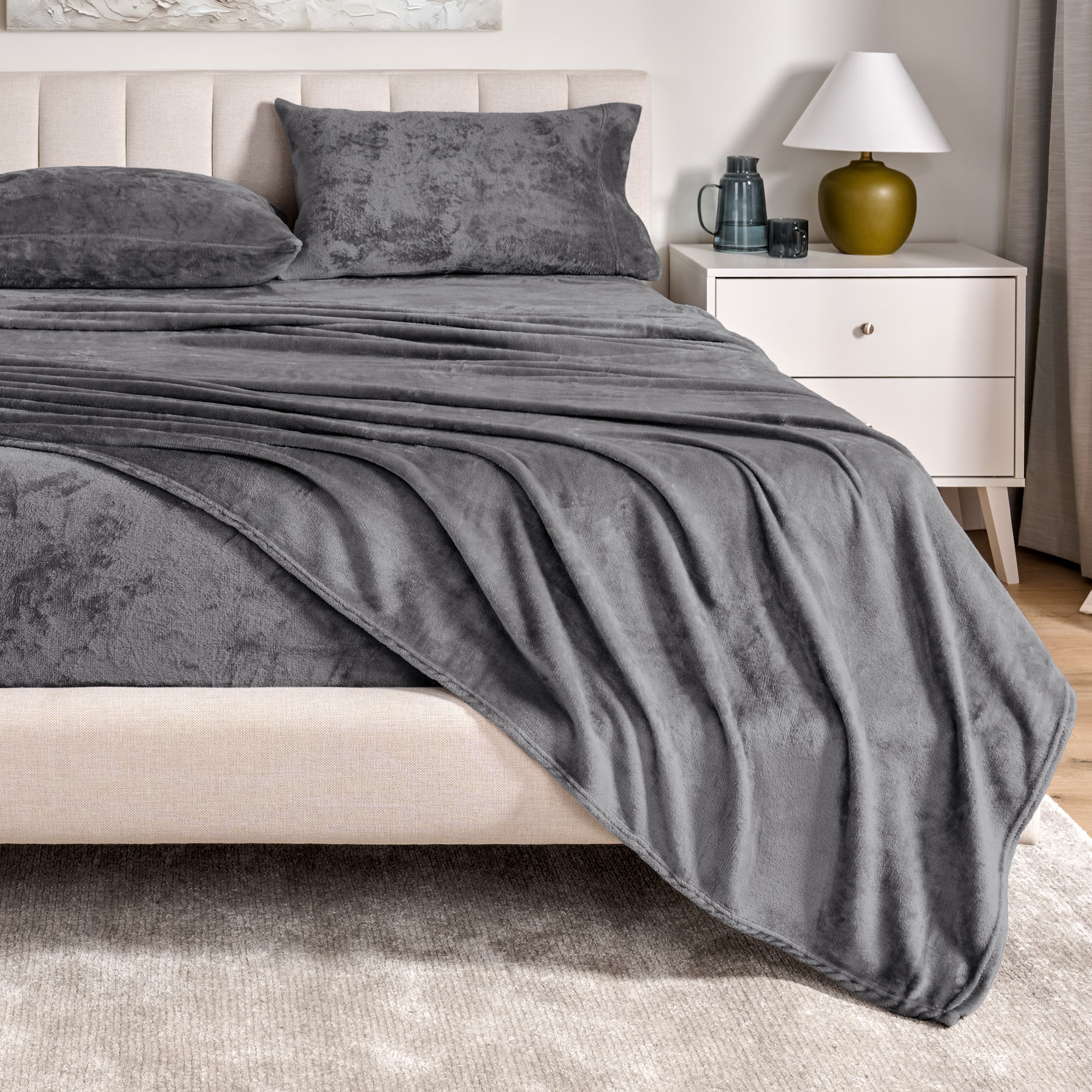Microplush sheets on a bed in a bedroom setting with a nightstand and lamp.