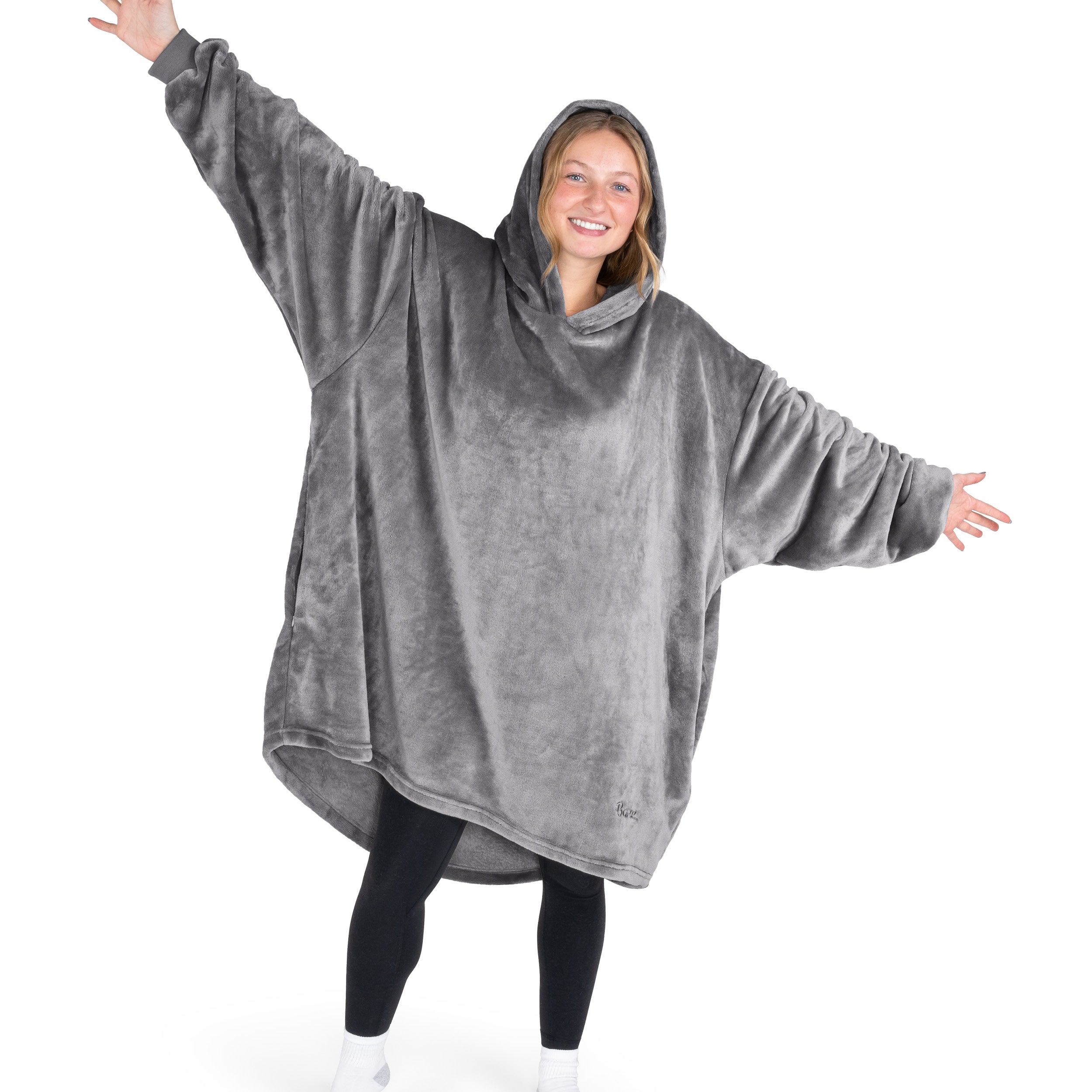 A woman is standing with her arms stretched out and has a hooded wearable blanket on