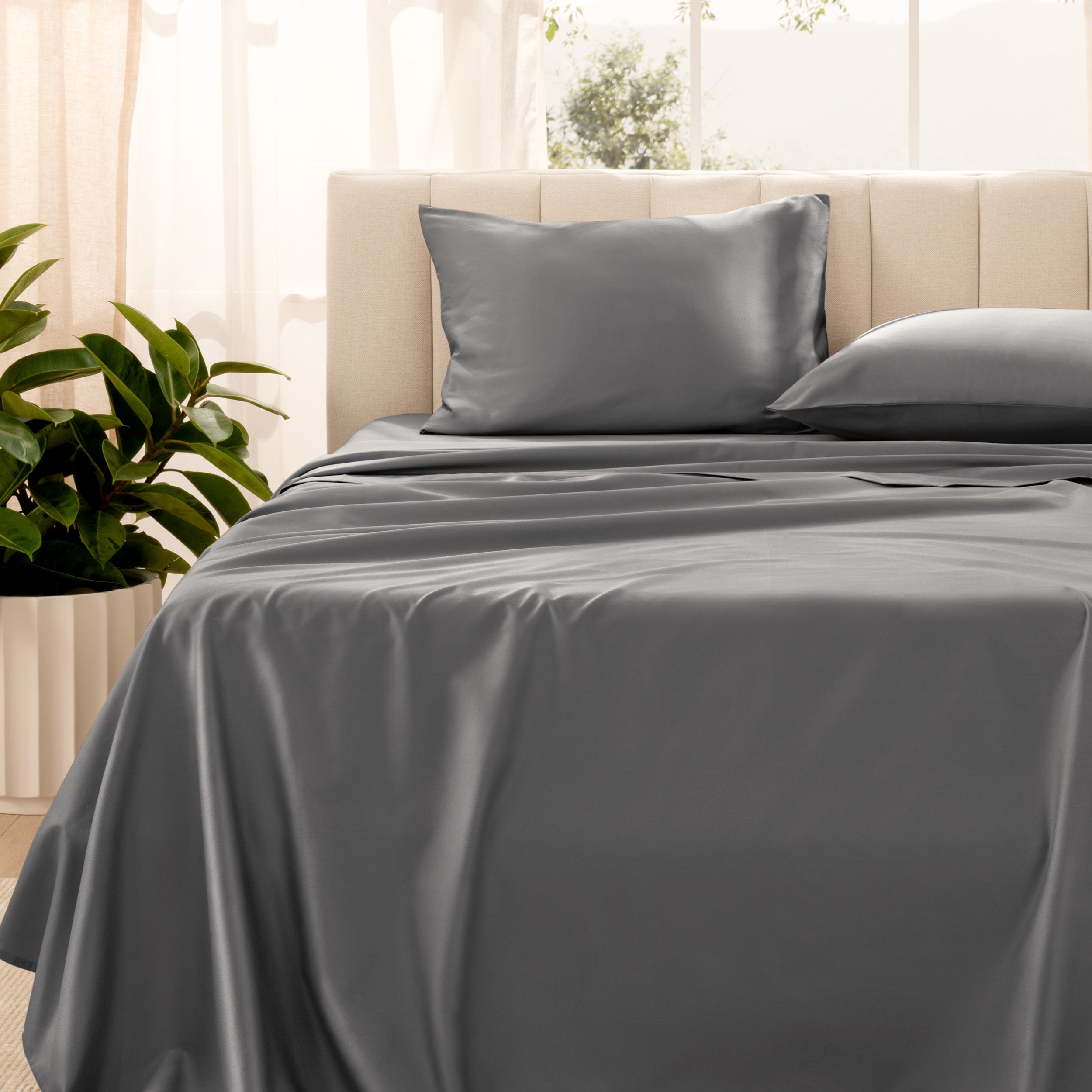 Organic sateen bedding on a bed with a beige headboard and plant in the corner.