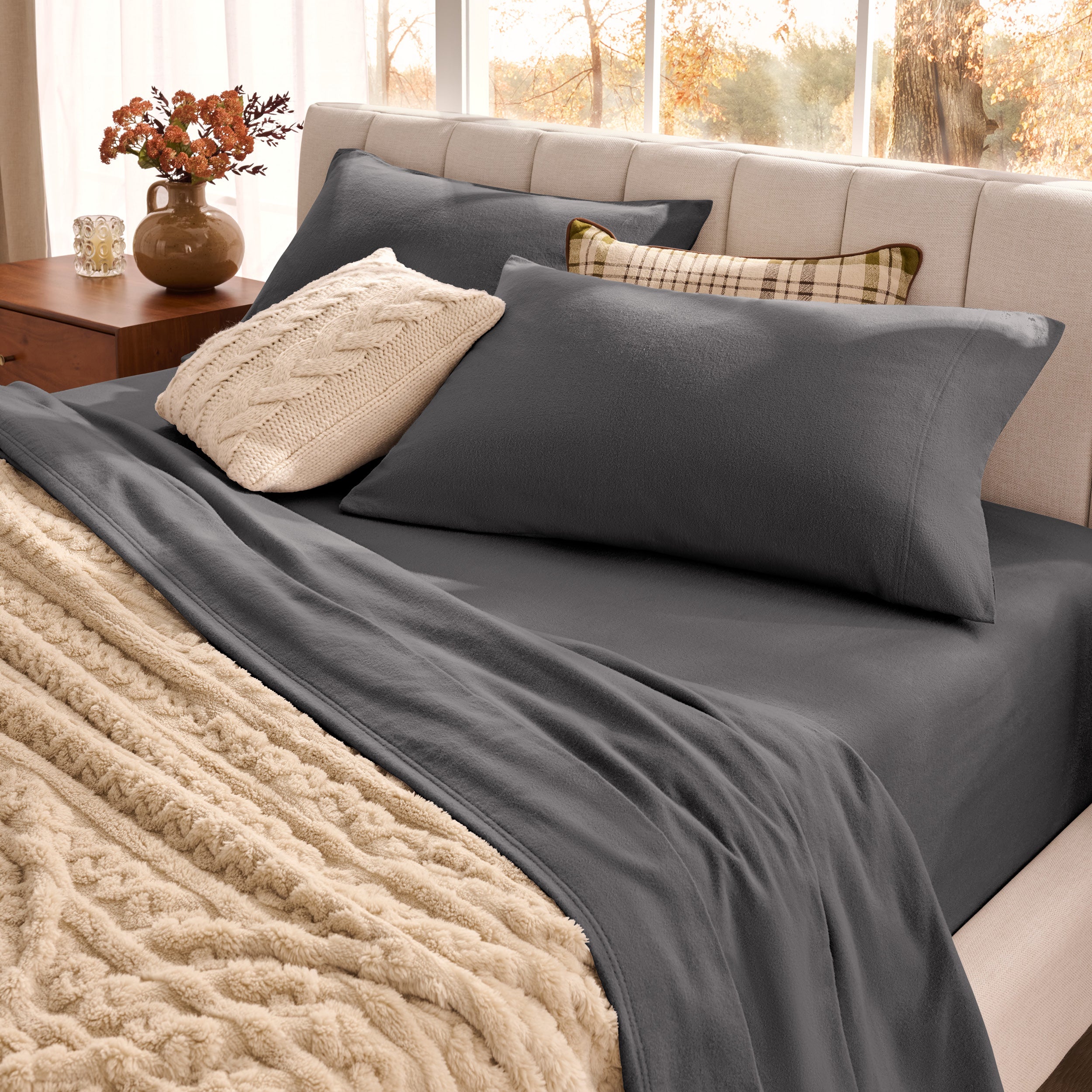 Neatly made bed with pillows and a beige blanket in a bright room.