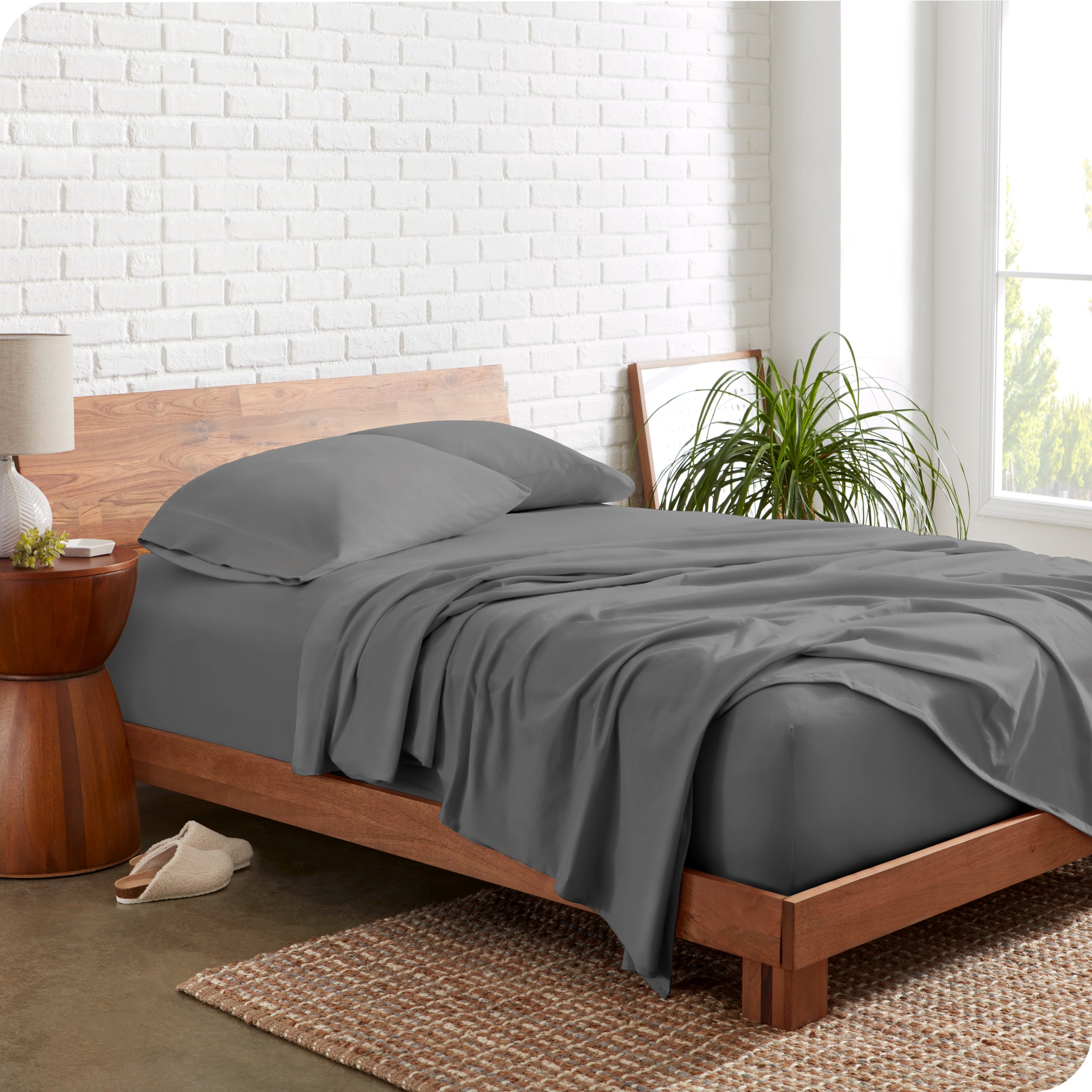 Organic jersey sheets on a bed with a brick wall behind the headboard