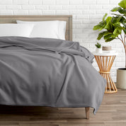 A polar fleece blanket on a bed next to a table and a large plant