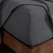 Corner of the bed with a fitted sheet on the mattress and a flat sheet draped over the side and end