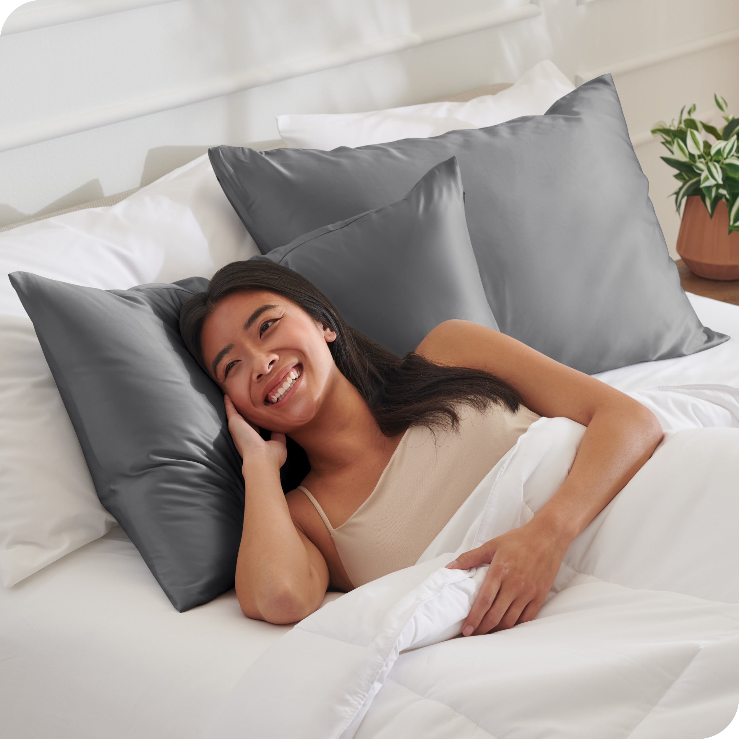 A woman in bed with her head resting on a silk pillowcase covered pillow