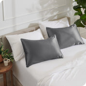 2 satin pillowcases on pillows leaning against other pillows on a bed