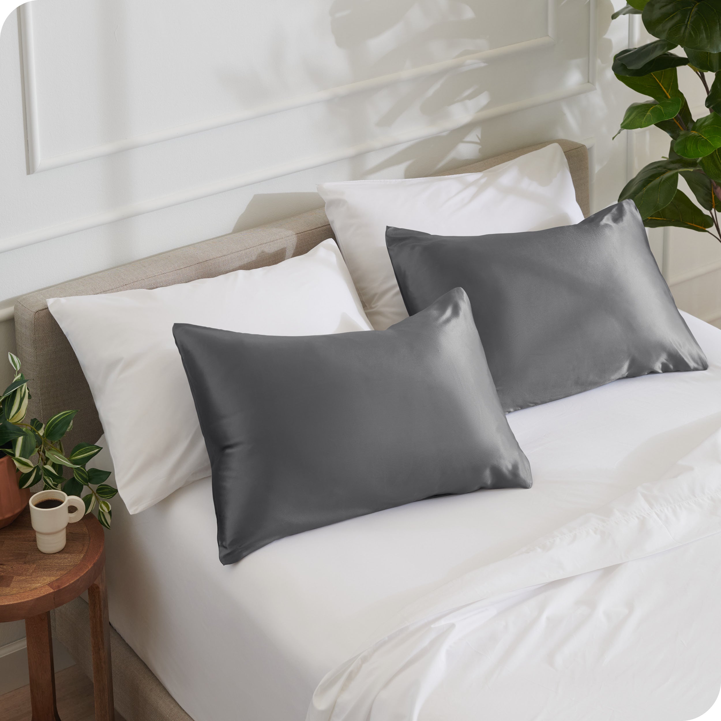 2 satin pillowcases on pillows leaning against other pillows on a bed