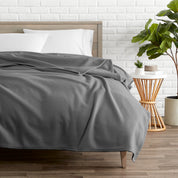 A polar fleece blanket on a bed next to a table and a large plant