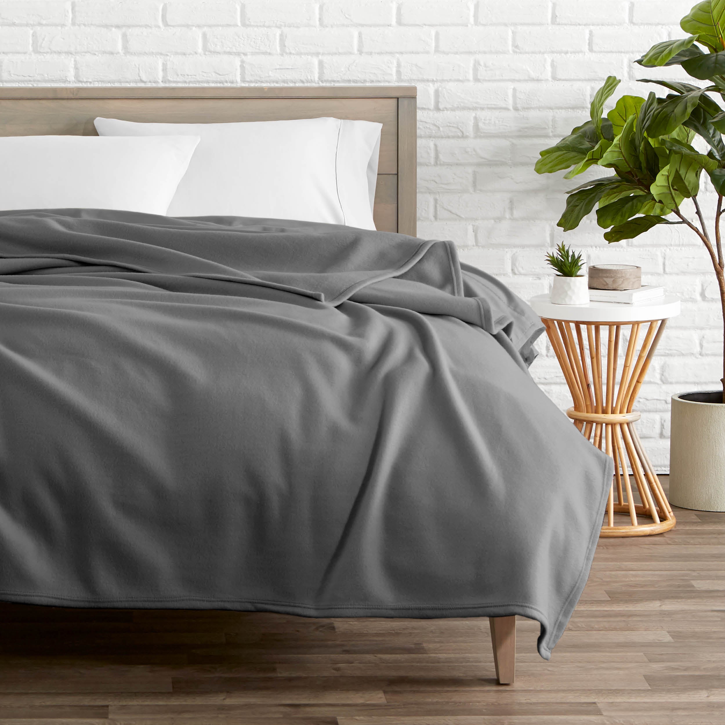 A polar fleece blanket on a bed next to a table and a large plant