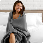 A woman sitting at the end of a bed with a fleece blanket wrapped around her shoulders