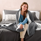 Woman cuddling with a sherpa blanket while sitting on the end of a bed