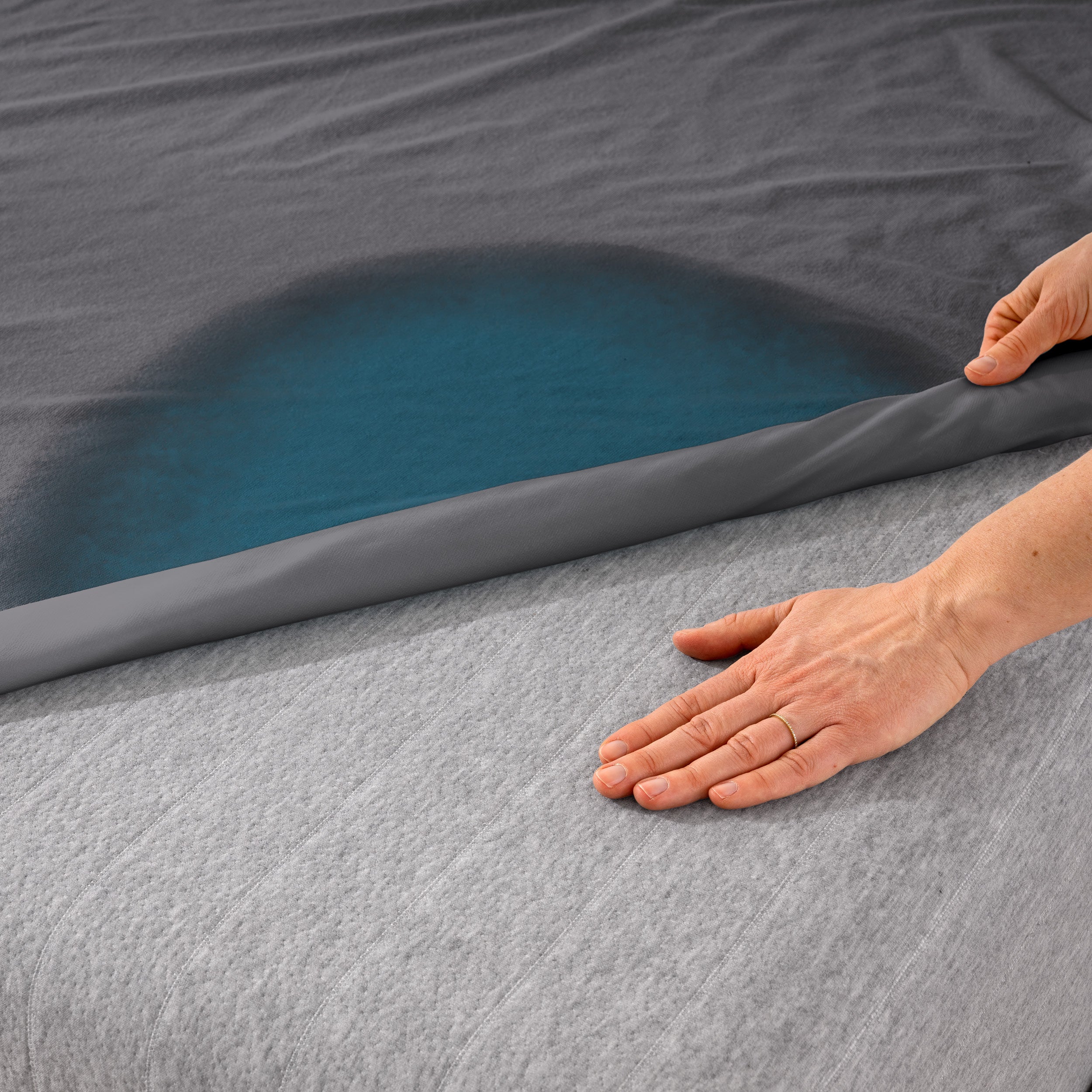 A hand is feeling the dry mattress underneath the wet mattress protector.