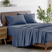 A wooden bed frame with heathered flannel sheets and pillowcases on the mattress