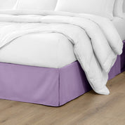 The corner of a bed with a bed skirt and comforter on it