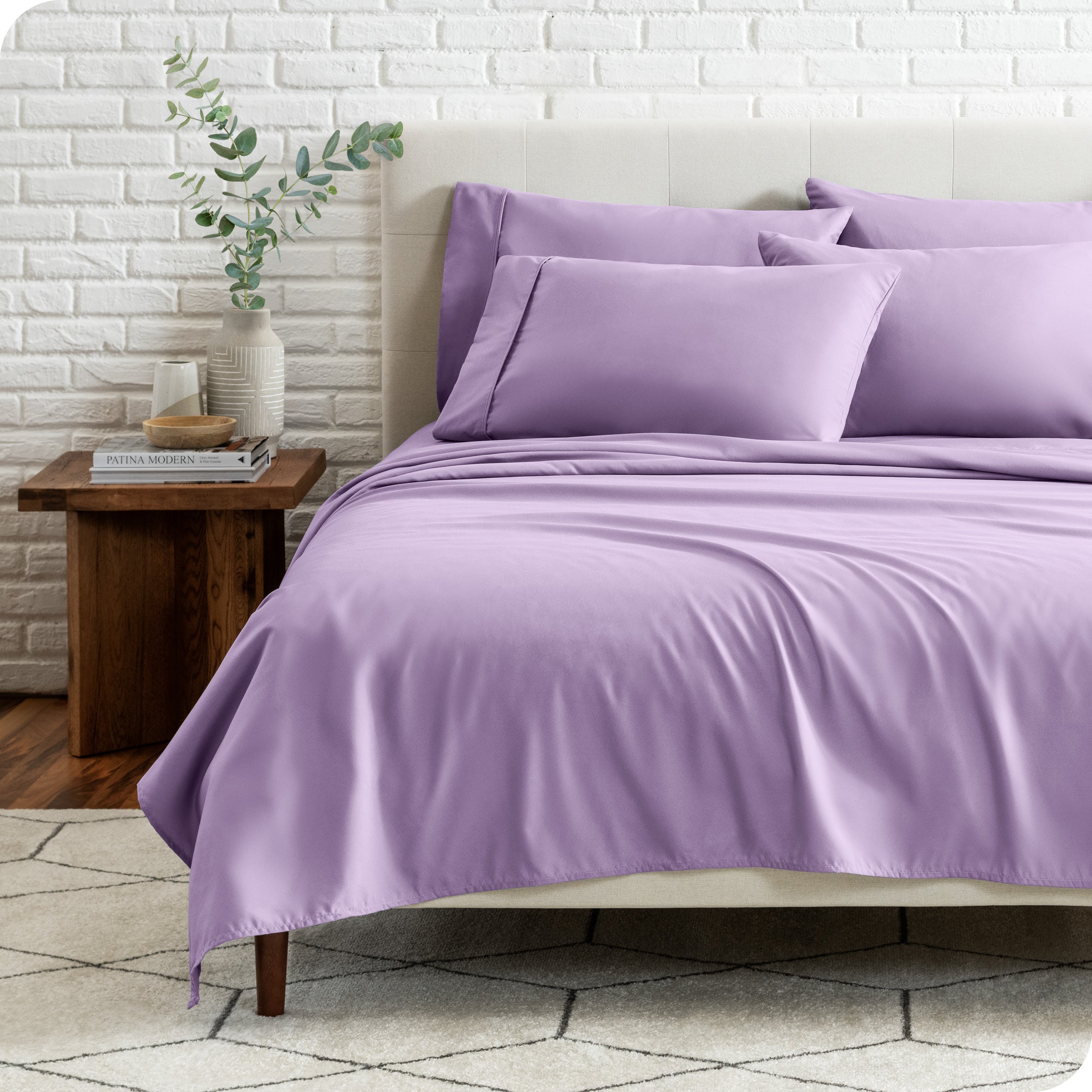 End view of a modern bed with the microfiber sheets on the bed with four pillows.