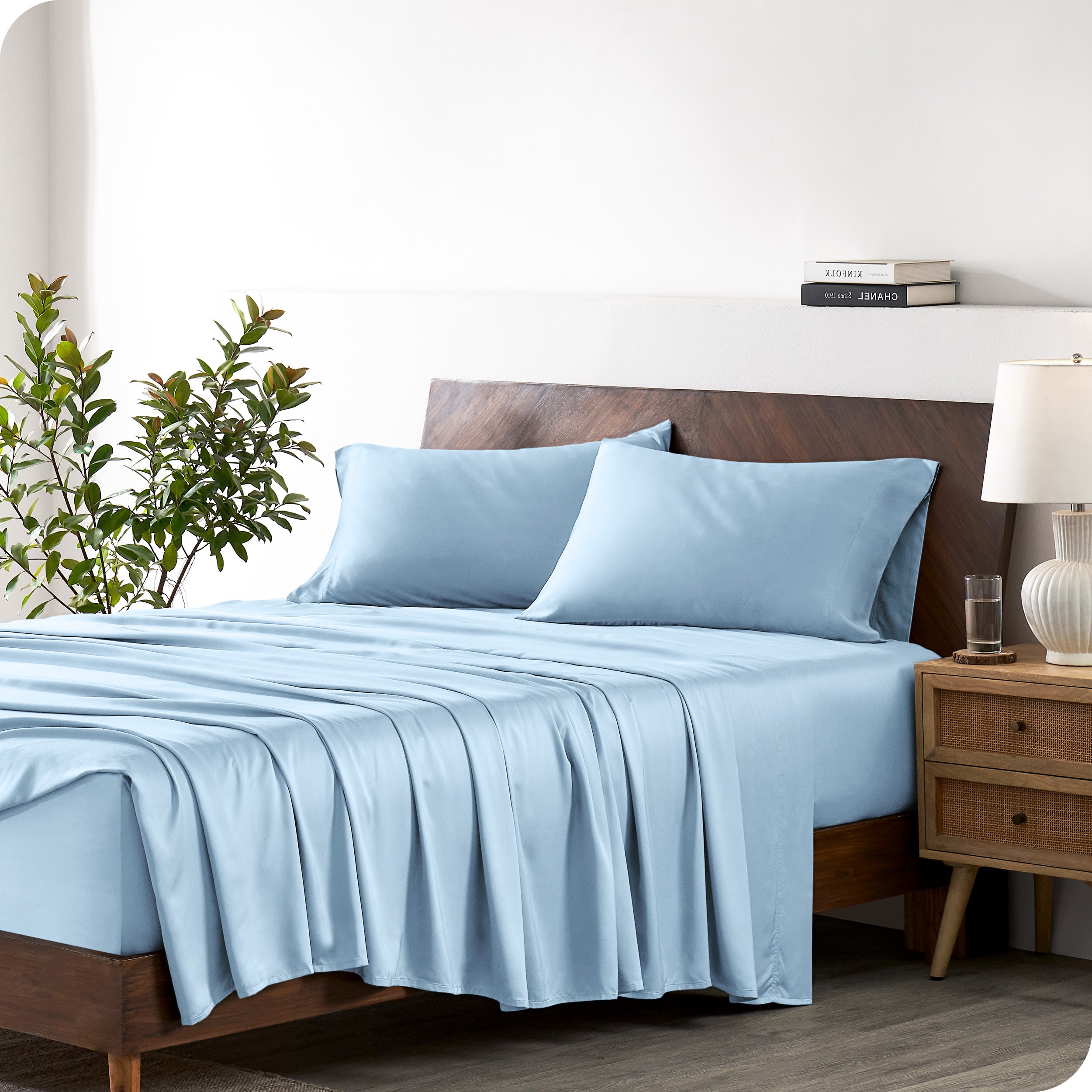 Modern bedroom with a bed against a white wall with a nightstand next to the bed. The bed has bamboo sheets draped over it.
