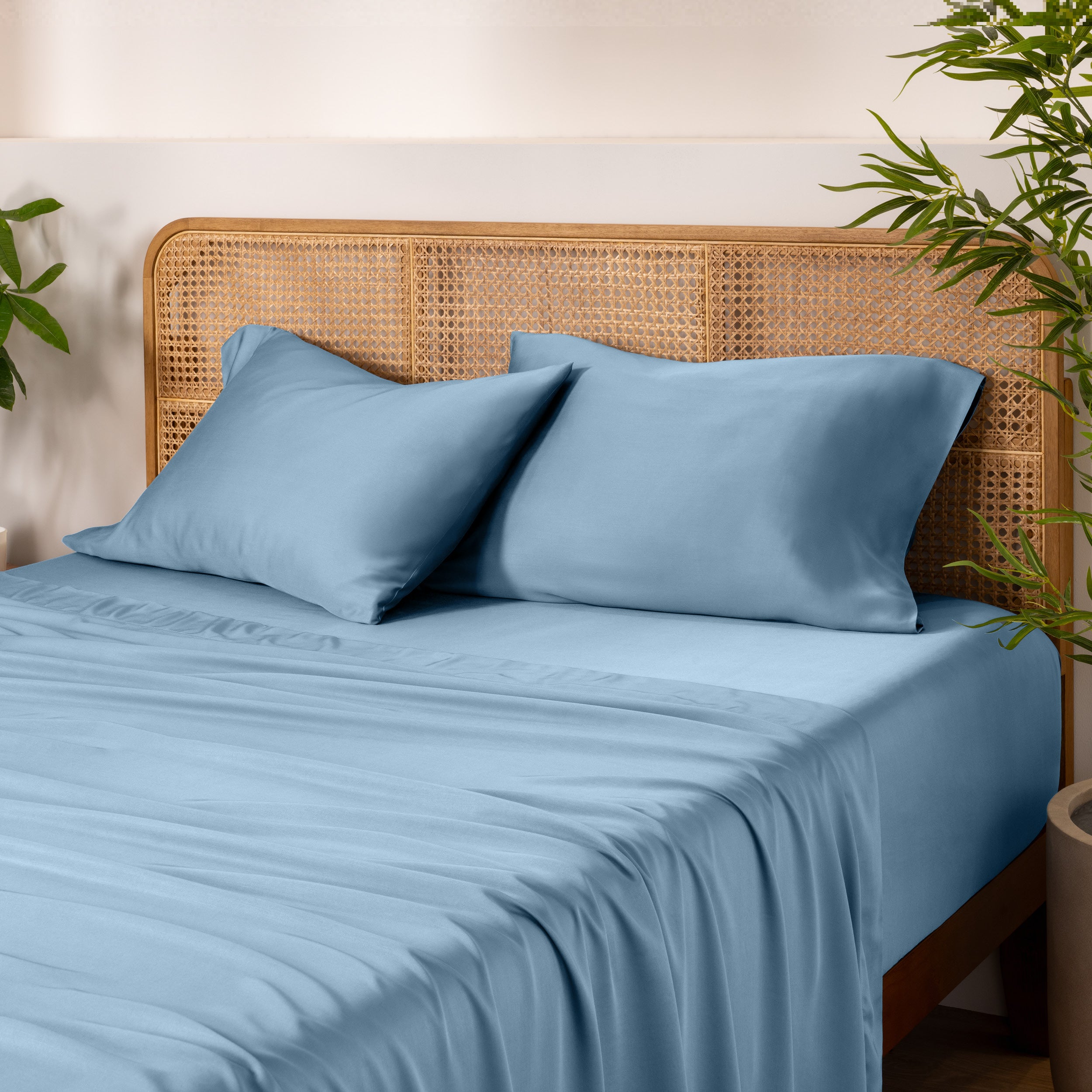 Bamboo bed sheets and pillowcases on a bed with a wicker headboard and plants in the background.