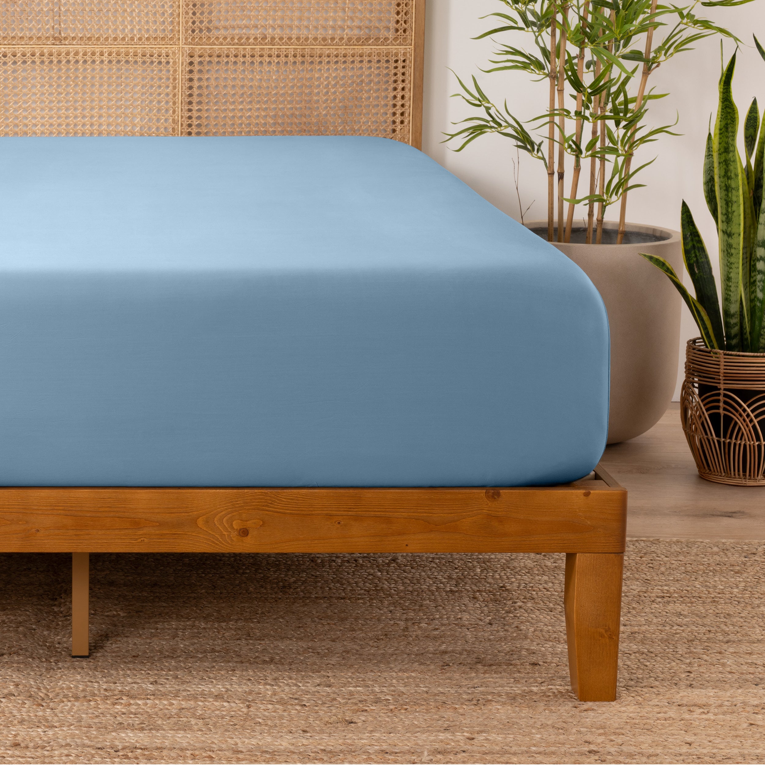 Bamboo fitted sheet on a wooden bed with plants in the background